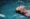 A person floats on their back in a swimming pool with eyes closed, surrounded by clear blue water, enjoying a sense of cleansing and renewal.
