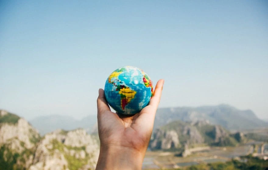 A person holds a small globe in their hand with a blurred landscape of mountains and sky in the background, symbolising the global rise of wellness trends like IV Vitamin Therapy.