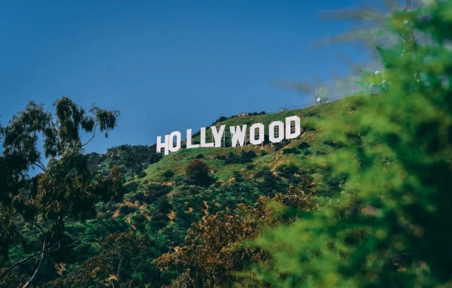 The Hollywood sign on a green hillside in Los Angeles, with blue sky and trees in the foreground—a landmark often visited by celebrities seeking wellness trends like IV vitamin drips.