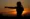 Silhouette of a person with one arm extended in a fist, standing outdoors at sunset, embracing the power of nature.
