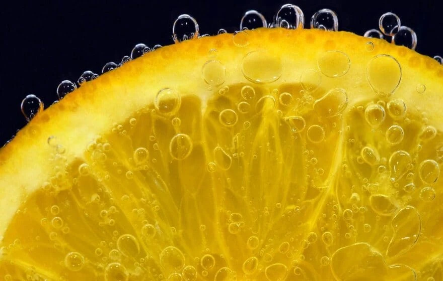 Close-up of a lemon slice with bubbles clinging to its surface against a black background, highlighting the vitamin C benefits found in citrus fruit.