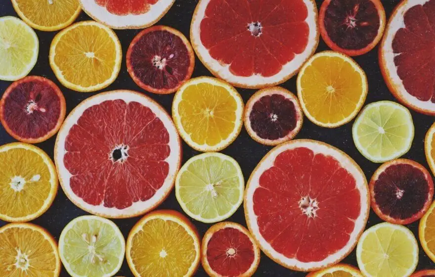 Assorted citrus fruit slices, including grapefruits, oranges, lemons, and blood oranges, arranged in a flat lay pattern on a dark background, showcasing natural Vitamin C benefits often found in Liposomal Vitamin C supplements.