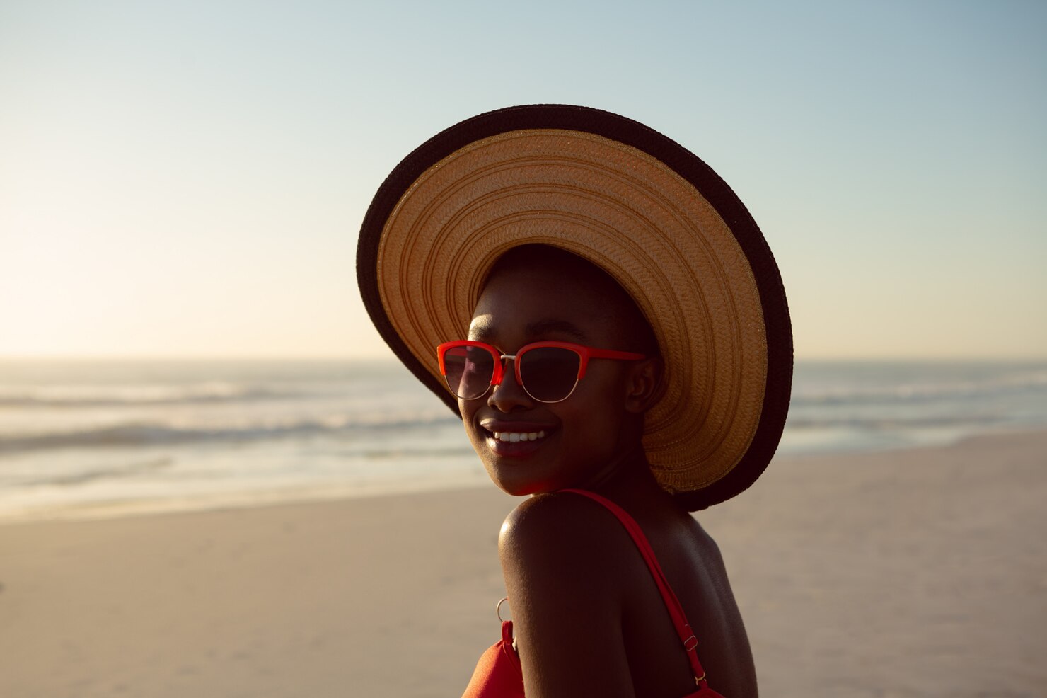 A woman in hat and sunglasses getting Vitamin D from the sun on the beach