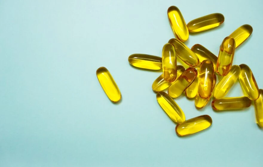 A group of yellow, translucent gel capsules—possibly arginine supplements—scattered on a light blue surface.