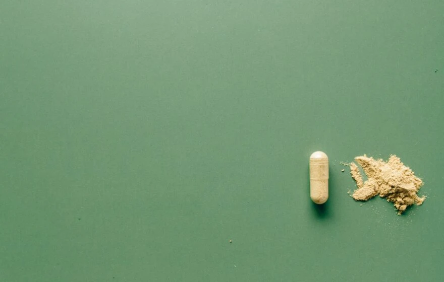 A beige capsule and a small pile of Alpha Lipoic Acid powder are displayed on a plain green surface.