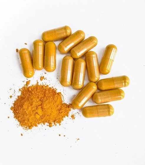Twelve yellow capsules, often found in curcumin supplements, are arranged on a white surface next to a small pile of yellow-orange powder.