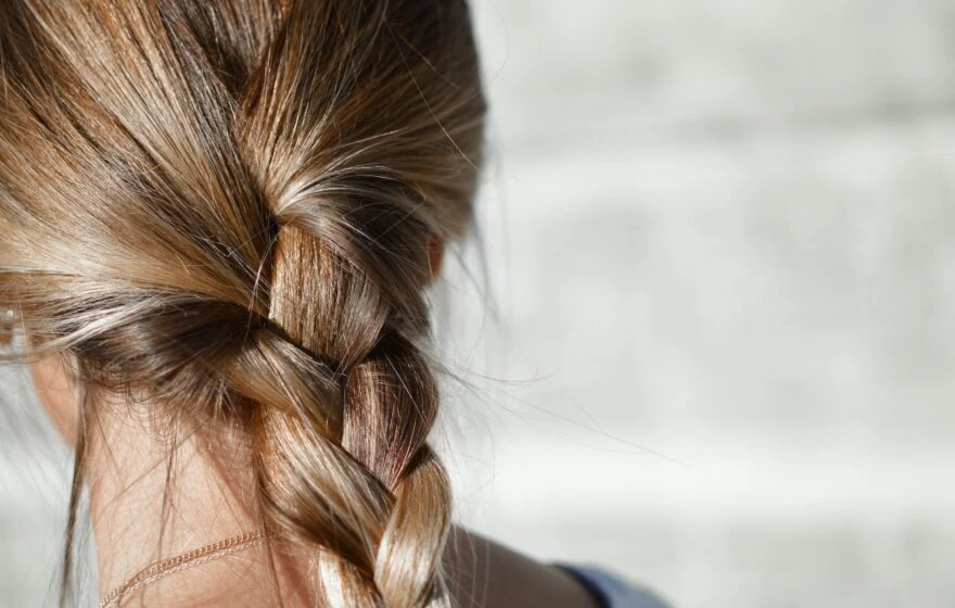Close-up view of the back of a person's head with light brown hair plaited loosely, highlighting healthy strands that may benefit from vitamins for hair growth, set against a blurred light-coloured background.