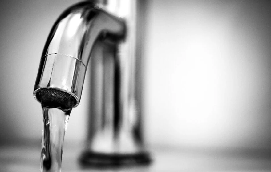 A close-up of a metal tap with water flowing from the spout, photographed in black and white—a reminder of how vital clean water is for preventing dehydration.