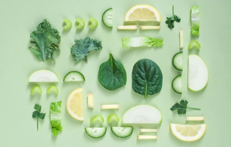 An assortment of sliced and whole green vegetables and lemon—among the best anti-inflammatory foods—arranged neatly on a light green background.