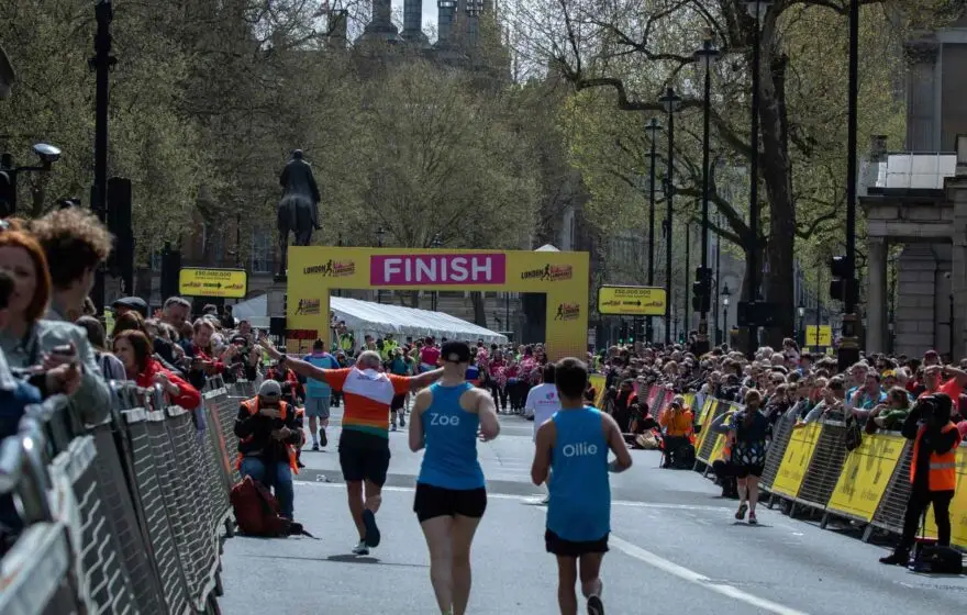 Marathon runners approach the finish line of a city marathon, with cheering crowds lined up behind barriers on both sides of the street, reminding everyone of the importance of proper marathon hydration.