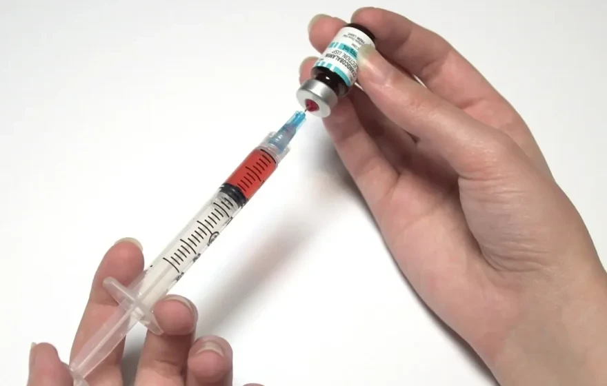 A person fills a syringe with liquid from a medical vial, preparing a Vitamin B12 injection against a white background.