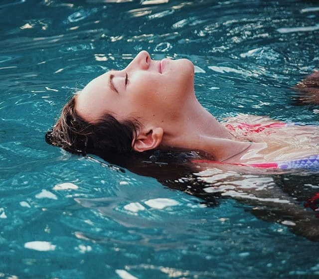 A person floats on their back in clear blue water with eyes closed, appearing relaxed and calm, as if experiencing deep rejuvenation from ozone therapy for detoxification.