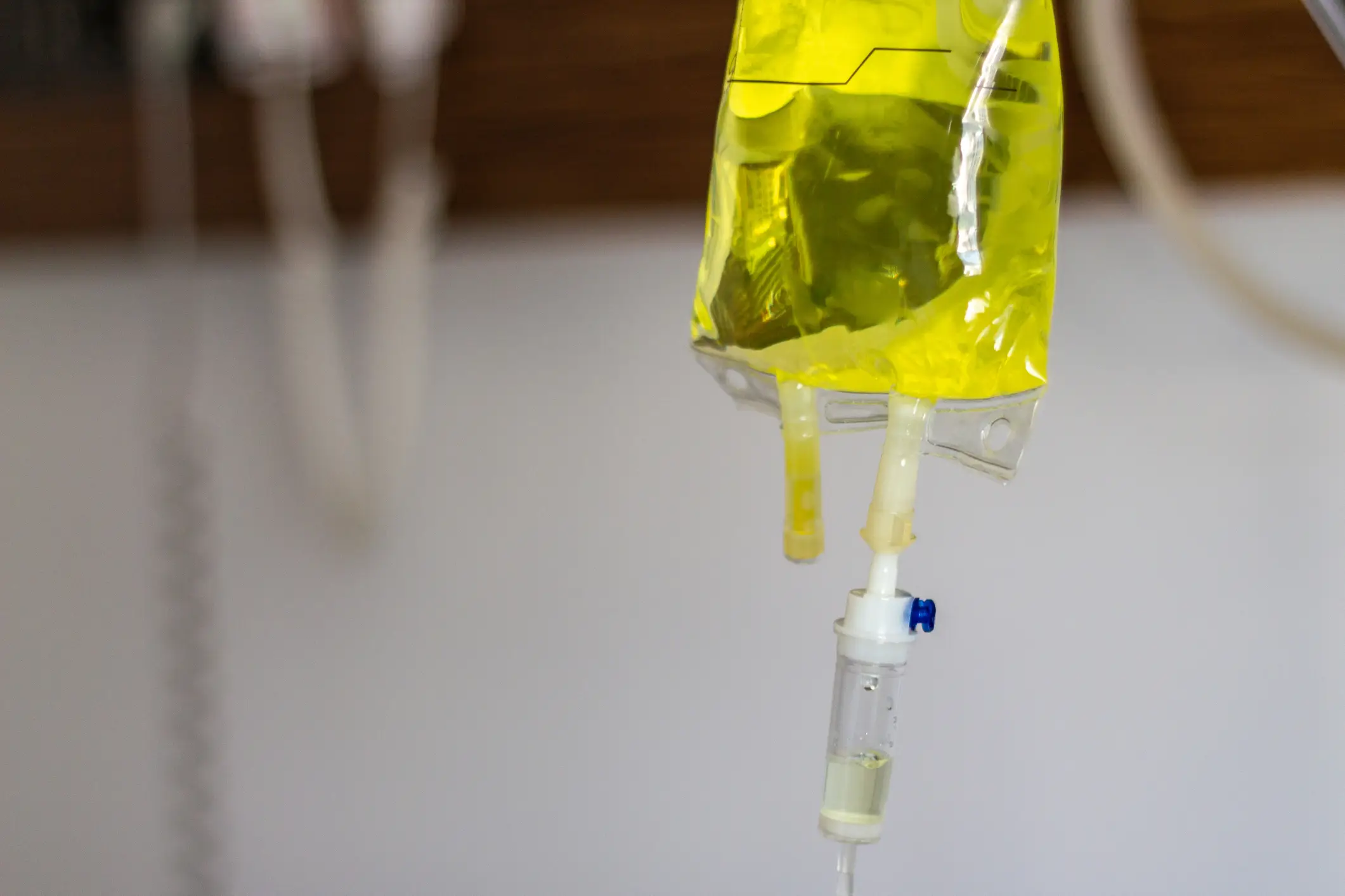 Close-up of a yellow intravenous (IV) fluid bag connected to a drip system, highlighting the power of IV drip therapy for medical treatment against a plain background.