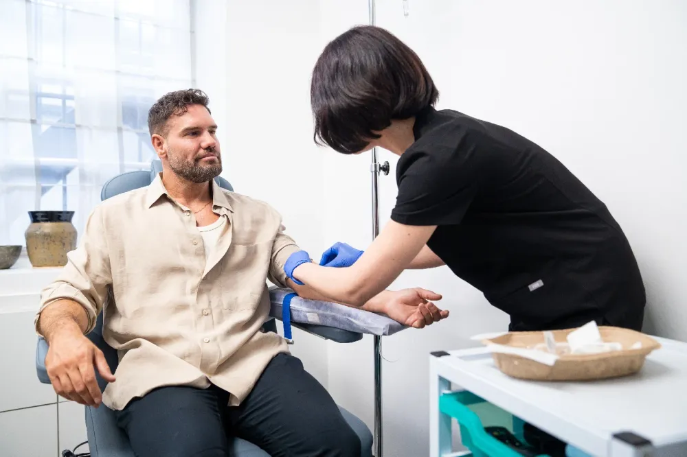 A healthcare worker prepares to take blood from a seated man’s arm in a medical examination room, highlighting the essential services provided in clinical settings.