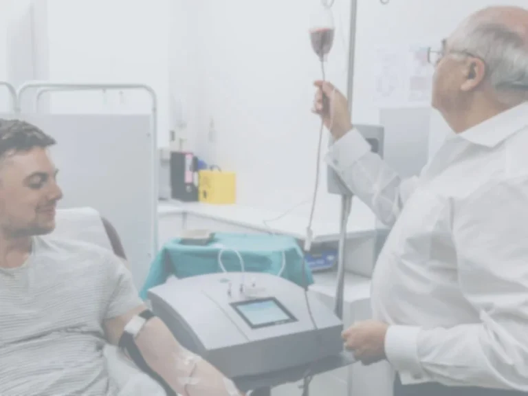 A man receives an ozone therapy infusion whilst sitting in a clinic as a healthcare professional monitors the IV drip.