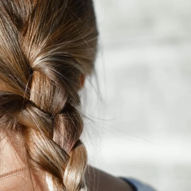 Close-up view of the back of a person's head with light brown hair plaited loosely, highlighting healthy strands that may benefit from vitamins for hair growth, set against a blurred light-coloured background.