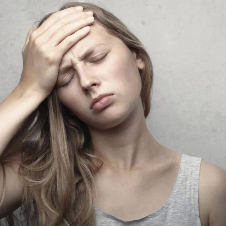 A young woman with long hair holds her hand to her forehead and closes her eyes, appearing to be in discomfort or pain—possibly in need of Vitamin B12 injections.
