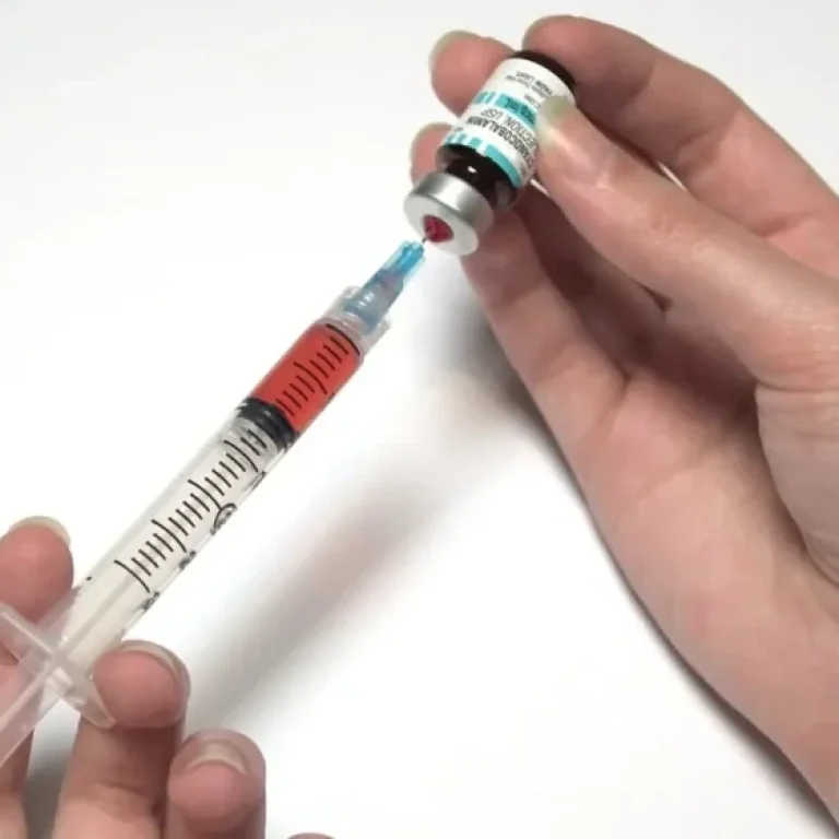 A person fills a syringe with liquid from a medical vial, preparing a Vitamin B12 injection against a white background.