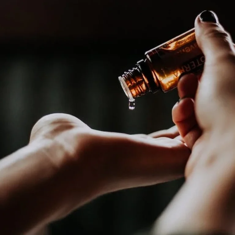 A person pours liquid from a small amber bottle onto their hand against a dark, blurred background, suggesting a step in their detox routine.