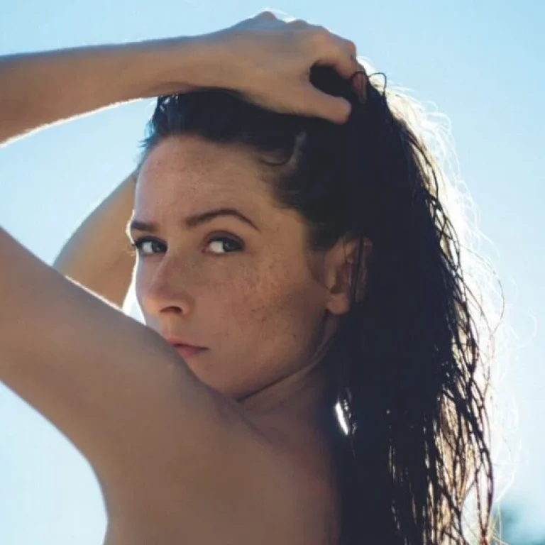 A woman with wet hair holds it back with one hand, looking over her shoulder towards the camera against a bright, sunlit background—a reminder of the importance of sunlight in preventing Vitamin D deficiency.