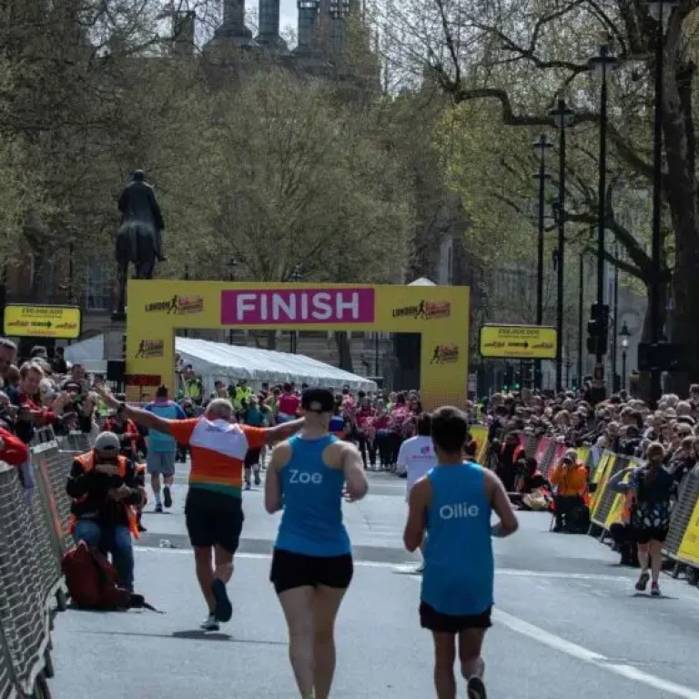 Marathon runners approach the finish line of a city marathon, with cheering crowds lined up behind barriers on both sides of the street, reminding everyone of the importance of proper marathon hydration.