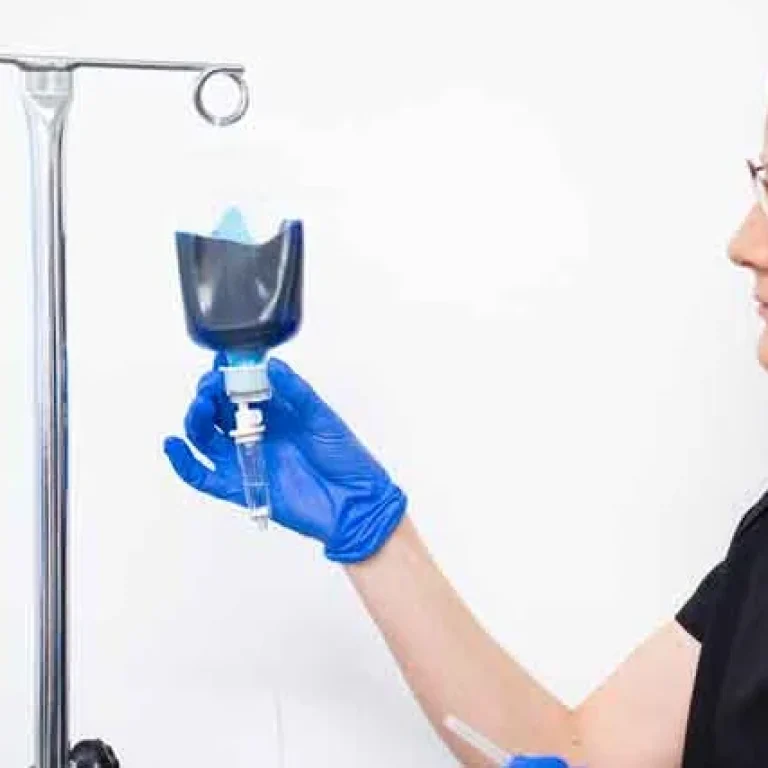 A person wearing blue gloves adjusts a Methylene Blue Infusion drip bag on a metal drip stand against a plain white background.
