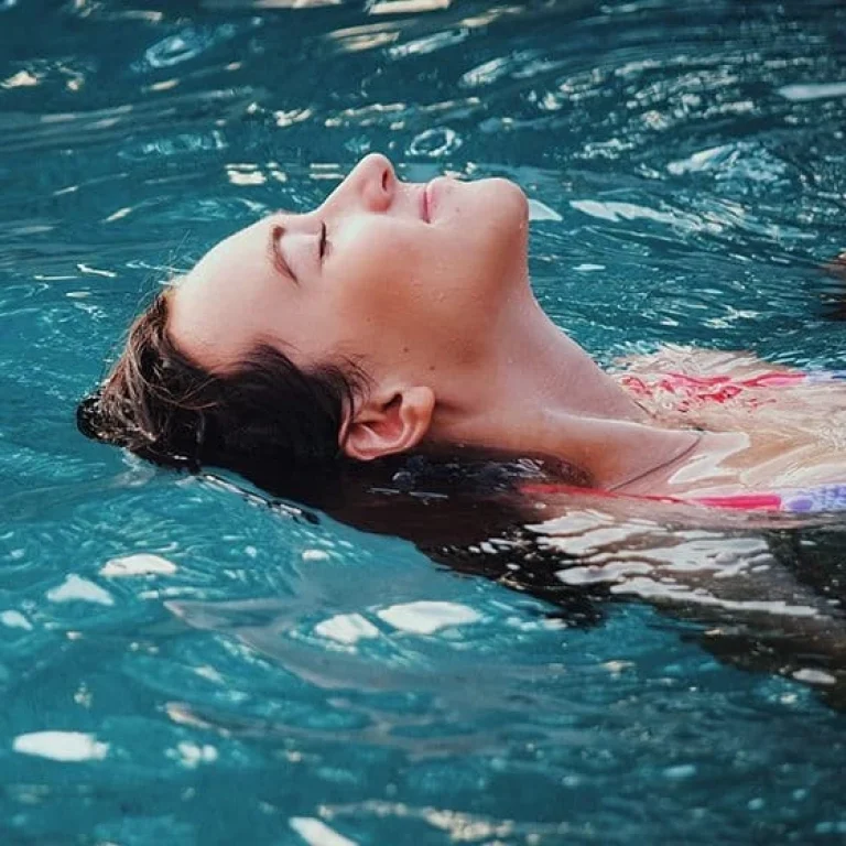 A person floats on their back in clear blue water with eyes closed, appearing relaxed and calm, as if experiencing deep rejuvenation from ozone therapy for detoxification.