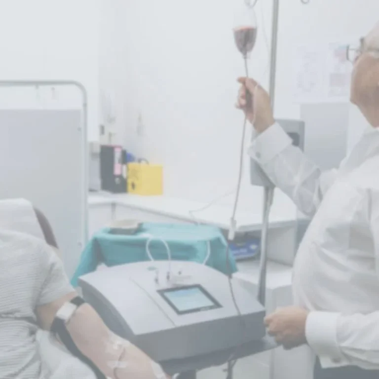 A man receives an ozone therapy infusion whilst sitting in a clinic as a healthcare professional monitors the IV drip.