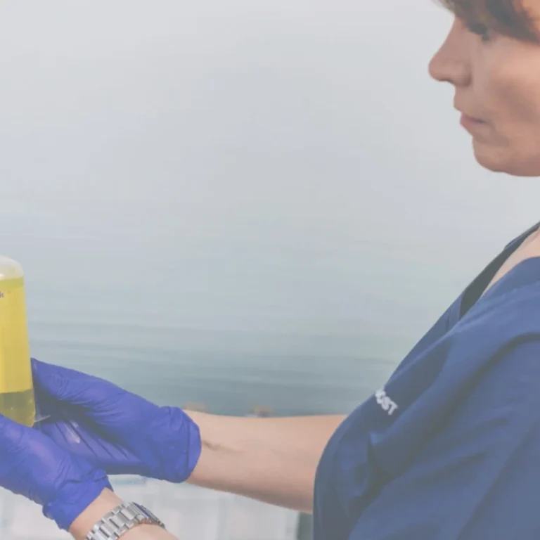 A person wearing blue gloves and scrubs holds a bottle labelled ivboost.uk containing yellow liquid, ready for an IV infusion as a potential performance booster.