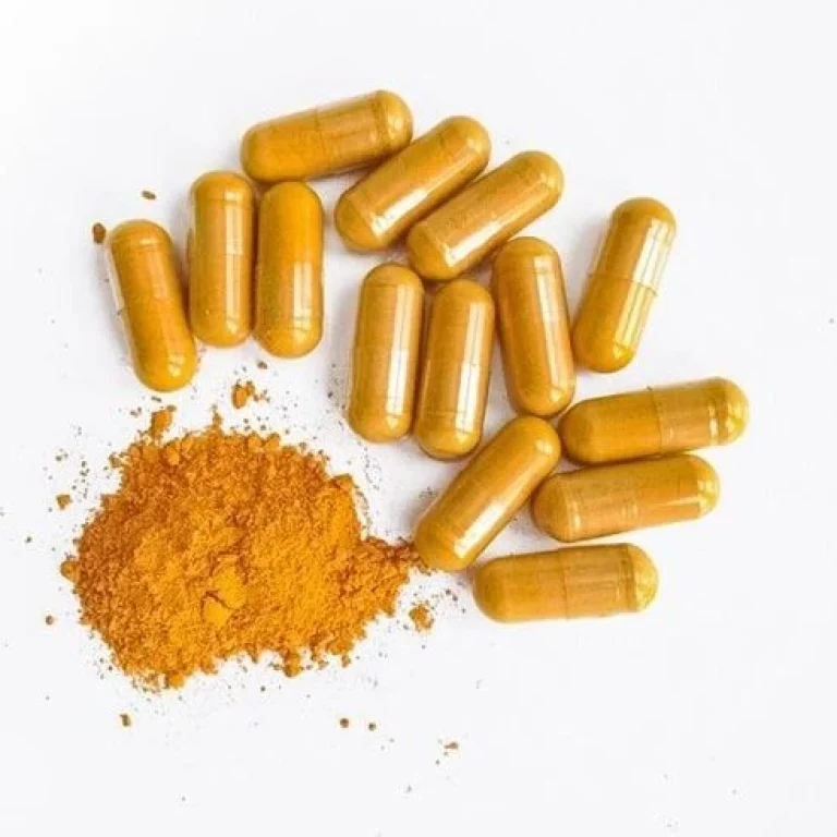 Twelve yellow capsules, often found in curcumin supplements, are arranged on a white surface next to a small pile of yellow-orange powder.