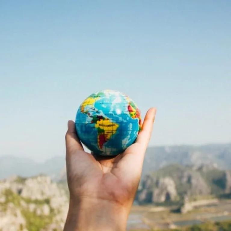 A person holds a small globe in their hand with a blurred landscape of mountains and sky in the background, symbolising the global rise of wellness trends like IV Vitamin Therapy.