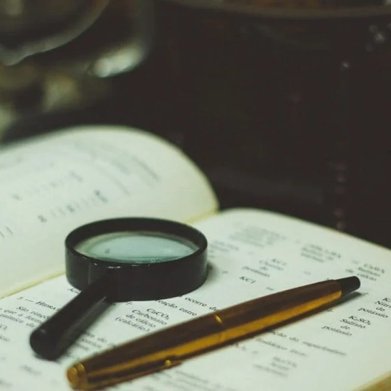 A magnifying glass and a pen rest on an open book filled with printed text, suggesting study or research activity—perhaps delving into the history of intravenous therapy or its development through the years.