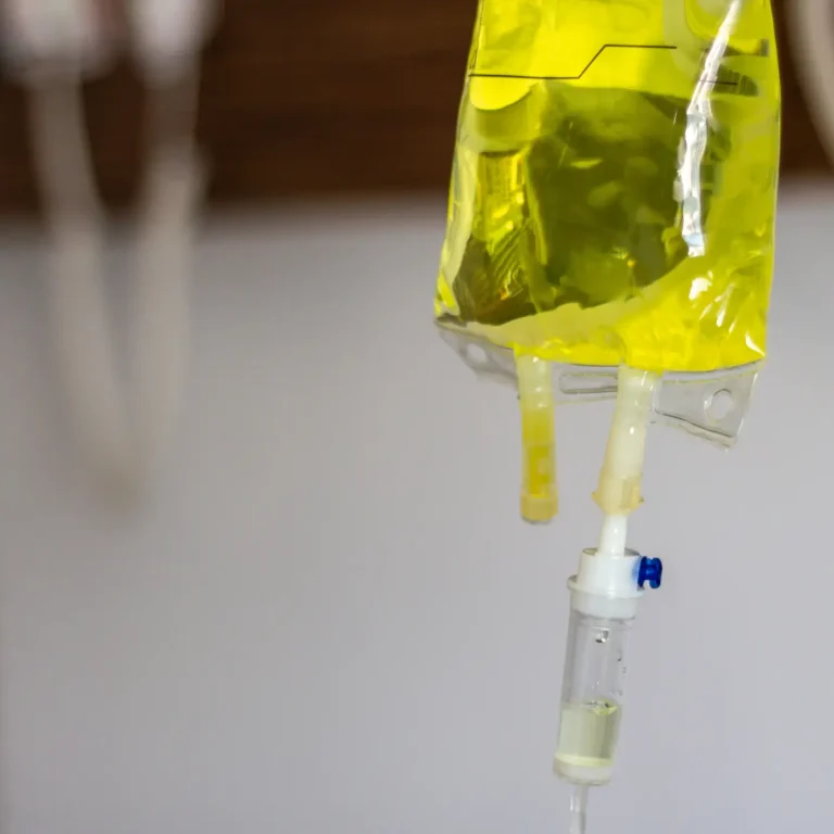 Close-up of a yellow intravenous (IV) fluid bag connected to a drip system, highlighting the power of IV drip therapy for medical treatment against a plain background.