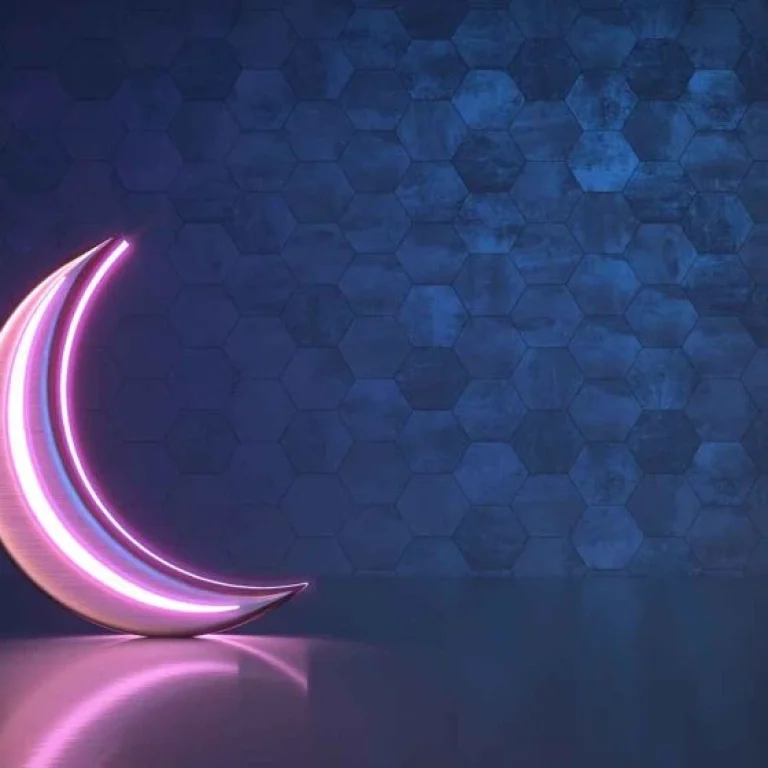 A pink neon crescent moon glows against a blue hexagonal-patterned wall, reflecting softly on a smooth surface—perfect inspiration for Ramadan fasting tips to help you ease out during the holy month.