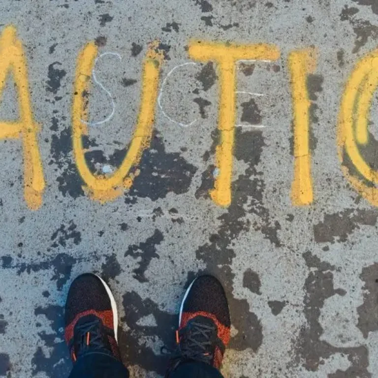 Yellow CAUTION is painted on worn pavement, partially seen from above, with a person's feet in trainers visible at the bottom—echoing caution around life expectancy trends similar to recent UK life expectancy concerns.