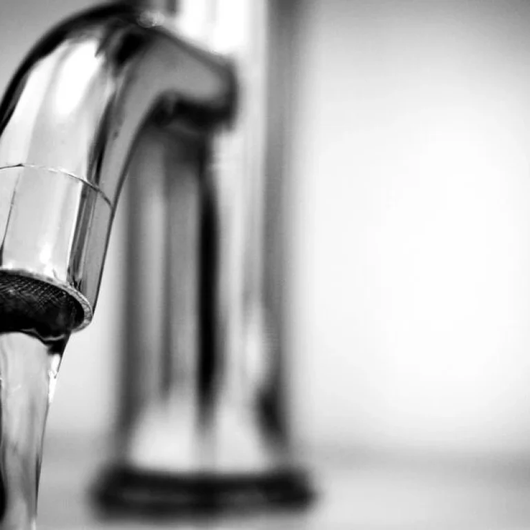 A close-up of a metal tap with water flowing from the spout, photographed in black and white—a reminder of how vital clean water is for preventing dehydration.