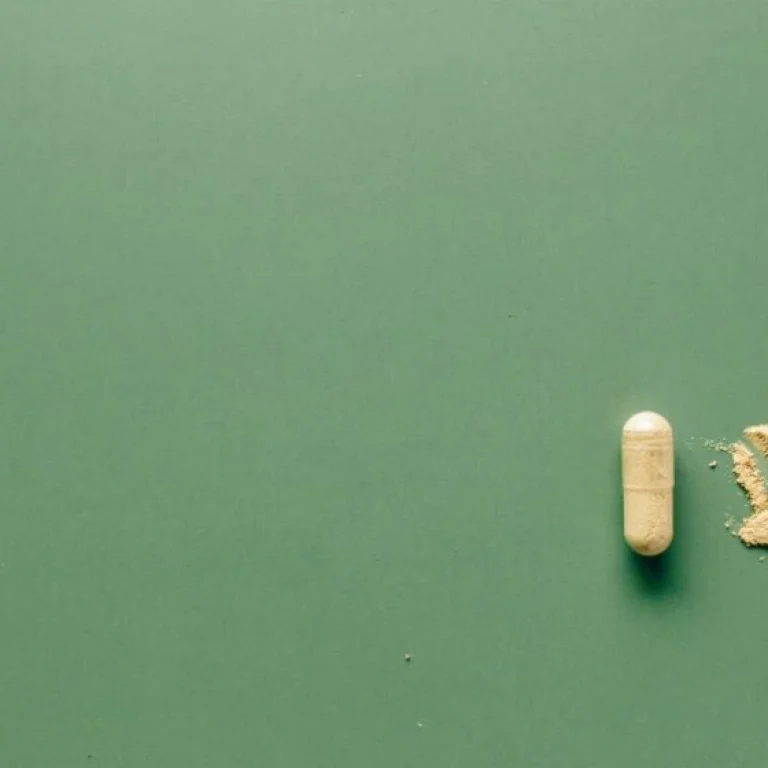 A beige capsule and a small pile of Alpha Lipoic Acid powder are displayed on a plain green surface.