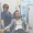 A nurse in blue scrubs assists a man receiving an IV therapy drip whilst seated in a medical clinic.